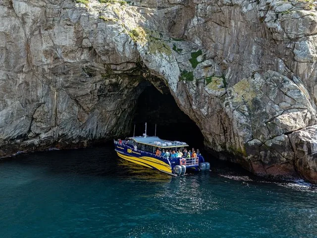 Ausflugsboot erkundet eine große Meereshöhle an einer rauen Felsenküste