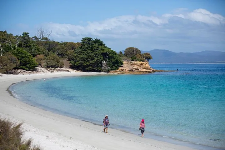 Two people walking along a white sand beach next to turquoise water