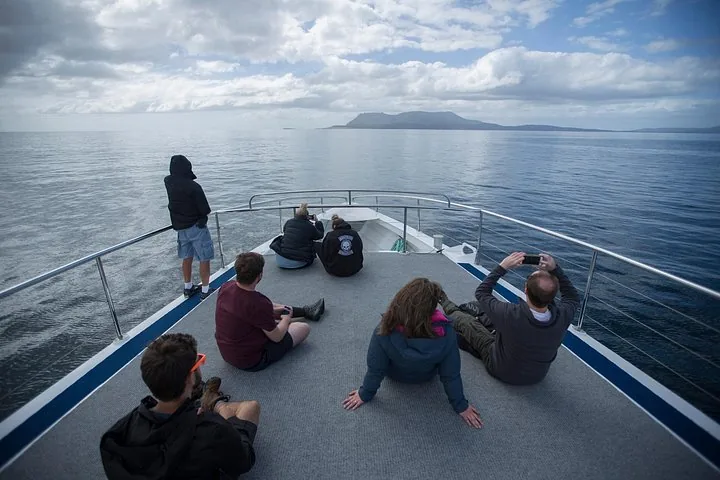 Passagiere entspannen auf dem Vorderdeck eines Bootes und blicken zur Insel